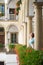 Young caucasian shorthair woman dressed in blue dress smiling while walking in italian courtyard