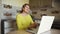 Young caucasian smiling woman with laptop communicates in online chat and social networks while at home in the kitchen.