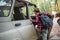 A young Caucasian woman with a backpack climbs into a jeep. Trees in the background. Side view. Concept of car travel and tourism