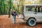 A young Caucasian woman with a backpack on her back closes the trunk of a jeep. In the background, trees and forest. Concept of