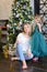 Young caucasian woman with bengal light wearing jeans and sitting with daughter near Christmas tree.