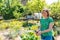 A young Caucasian woman cheerfully waters the beds with greenery with a hose.Summer. The concept of gardening and summer