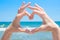 Young Caucasian Woman Girl Making Heart with Hands Palms. Turquoise Sea with Waves Blue Sky Horizon Background. Bright Sunlight