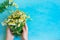 Young Caucasian Woman Hold Bouquet of Freshly Picked Camomile Flowers Tied with Twine on Light Blue Wood Table. Beauty Skin Care