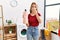 Young caucasian woman holding detergent bottle at laundry room covering mouth with hand, shocked and afraid for mistake