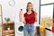 Young caucasian woman holding detergent bottle at laundry room smiling with an idea or question pointing finger with happy face,