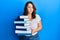 Young caucasian woman holding a pile of books puffing cheeks with funny face