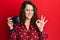 Young caucasian woman holding reflex camera doing ok sign with fingers, smiling friendly gesturing excellent symbol