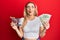 Young caucasian woman holding small supermarket shopping cart and dollars making fish face with mouth and squinting eyes, crazy