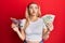 Young caucasian woman holding small supermarket shopping cart and dollars puffing cheeks with funny face