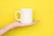 Young Caucasian Woman Holds on Hand Palm Blank Mockup White Mug on Bright Yellow Painted Wall. Airy Breezy Style