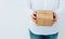 Young caucasian woman in jeans shirt holds in hands gift box wrapped in brown craft paper tied with twine. White wall. Christmas