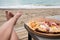 Young Caucasian woman lying at the beach eating pizza. Legs and Italian food slices, sea in background. Careless holidays at all
