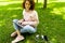 Young caucasian woman with perfect smile, plump lips, glasses walks in nature, sits on a grass with laptop and