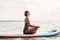 Young Caucasian woman practicing yoga on paddle sup surfboard at sunset. Female stretching doing workout on a lake river water.