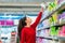 A young Caucasian woman reaches to the top shelf for a pack of sanitary pads. Side view. The concept of purchasing