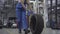 Young caucasian woman rolling tire in repair shop. Smiling female auto mechanic at workplace. Camera zooming down