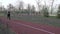 A young Caucasian woman runs along a red rubber track through a park. Girl athlete doing cardio workout in the city