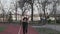 A young Caucasian woman runs along a red rubber track through a park. Girl athlete doing cardio workout in the city