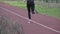 A young Caucasian woman runs along a red rubber track through a park. Girl athlete doing cardio workout in the city