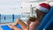 Young Caucasian Woman in Santa Claus Hat Drinking Coconut on Sunbed