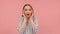 Young caucasian woman in shock holding fingertips on temples and looking on the side, isolated on pink background