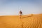 Young caucasian woman in shorts and t-shirt going away towards the arabian desert dunes, footprints and ripples in the sand.