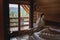 Young caucasian woman sitting on a bed in a wooden chalet cabin in the mountains. Comfortable rest and sleep in a log house in