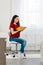 A young Caucasian woman is sitting in a bright room on a chair and reading a book. Copy space. Vertical. There is a large window