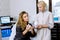 Young Caucasian woman sitting on couch while female doctor cosmetologist showing new cream and lotion for professional