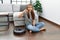 Young caucasian woman sitting at home by vacuum robot with angry face, negative sign showing dislike with thumbs down, rejection