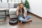 Young caucasian woman sitting at home by vacuum robot doing ok sign with fingers, smiling friendly gesturing excellent symbol