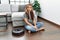 Young caucasian woman sitting at home by vacuum robot thinking attitude and sober expression looking self confident
