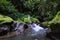 Young Caucasian woman sitting on the rock near the river in Vajrasana or Diamond pose. Hands in gyan mudra. Tropical nature