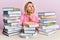 Young caucasian woman sitting on the table with books thinking concentrated about doubt with finger on chin and looking up