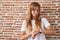 Young caucasian woman standing over bricks wall checking the time on wrist watch, relaxed and confident