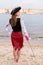 Young Caucasian woman in striped pirate costume lowered toy sword down on beach