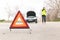 Young Caucasian woman, talking on her cell phone while her car is broken down on the road with reflective warning triangles.