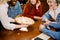 Young Caucasian woman waitress bringing pizza for group of diverse multiracial friends in cafe.