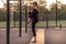 Young caucasian woman warms up on the park sport ground. The girl in a sports pose leg up at the cover, in black sportswear.