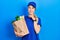 Young caucasian woman wearing courier uniform with groceries from supermarket with hand on chin thinking about question, pensive
