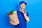 Young caucasian woman wearing courier uniform with groceries from supermarket hand on mouth telling secret rumor, whispering