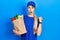 Young caucasian woman wearing courier uniform with groceries from supermarket surprised pointing with hand finger to the side,