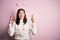 Young caucasian woman wearing cute easter rabbit ears over pink isolated background gesturing finger crossed smiling with hope and
