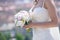 Young Caucasian woman wearing an embroidered wedding dress and holding a round peonies bouquet, an essential accessory for a bride