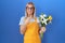 Young caucasian woman wearing florist apron holding flowers pointing aside worried and nervous with forefinger, concerned and