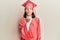 Young caucasian woman wearing graduation cap and ceremony robe looking at the camera blowing a kiss with hand on air being lovely