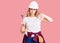 Young caucasian woman wearing hardhat holding wrench with angry face, negative sign showing dislike with thumbs down, rejection