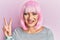 Young caucasian woman wearing pink wig smiling with happy face winking at the camera doing victory sign