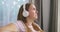 A young Caucasian woman wearing wireless headphones sits on a couch at home